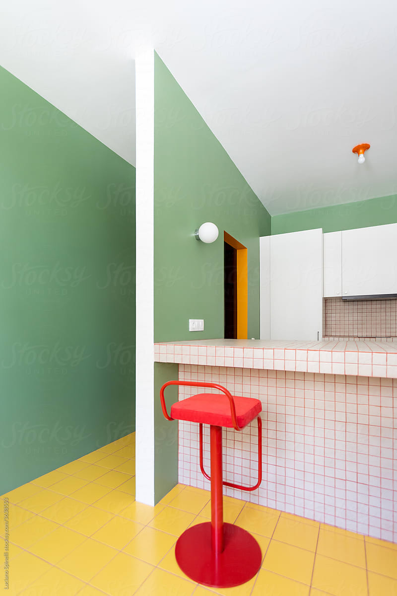 Red stool and white countertop in a green minimalist kitchen next to a corridor