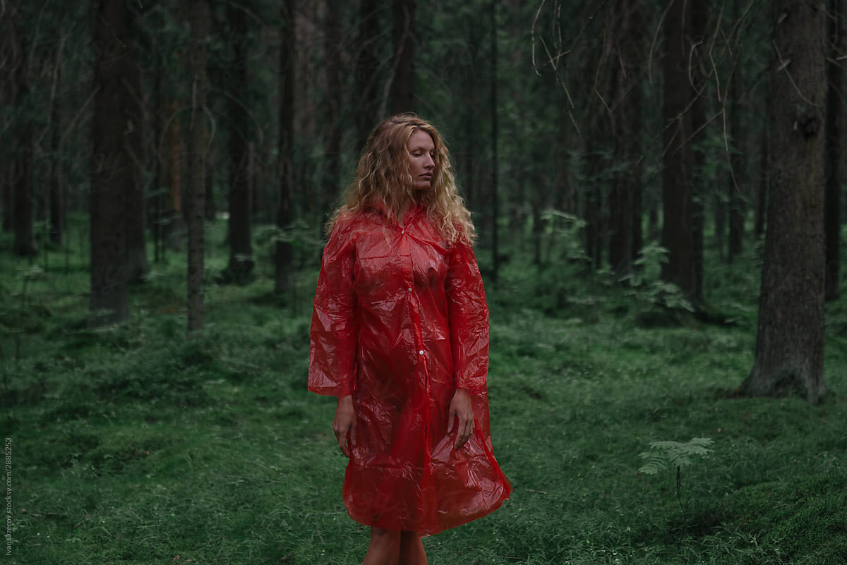 a woman in a red raincoat stands in a gloomy forest