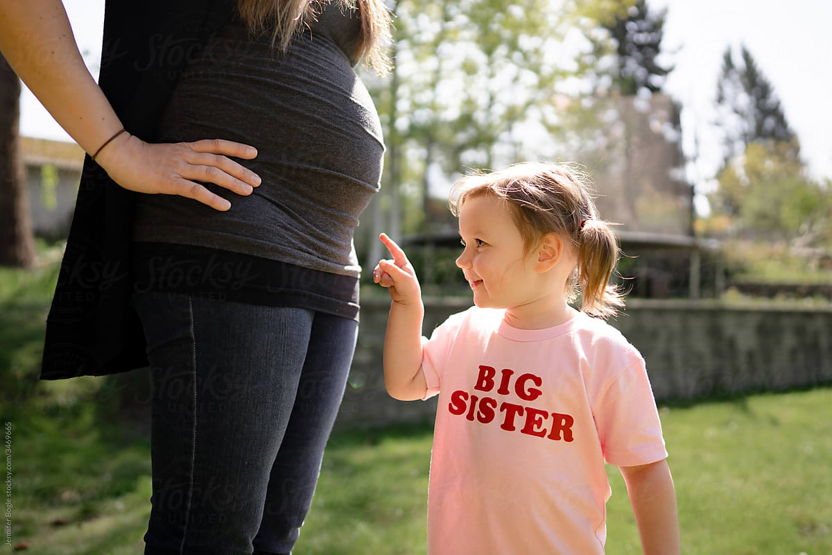 Girl in big sister shirt points at mom\'s pregnant belly