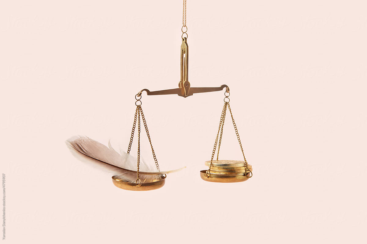 Golden coins and feather on weighing scale.