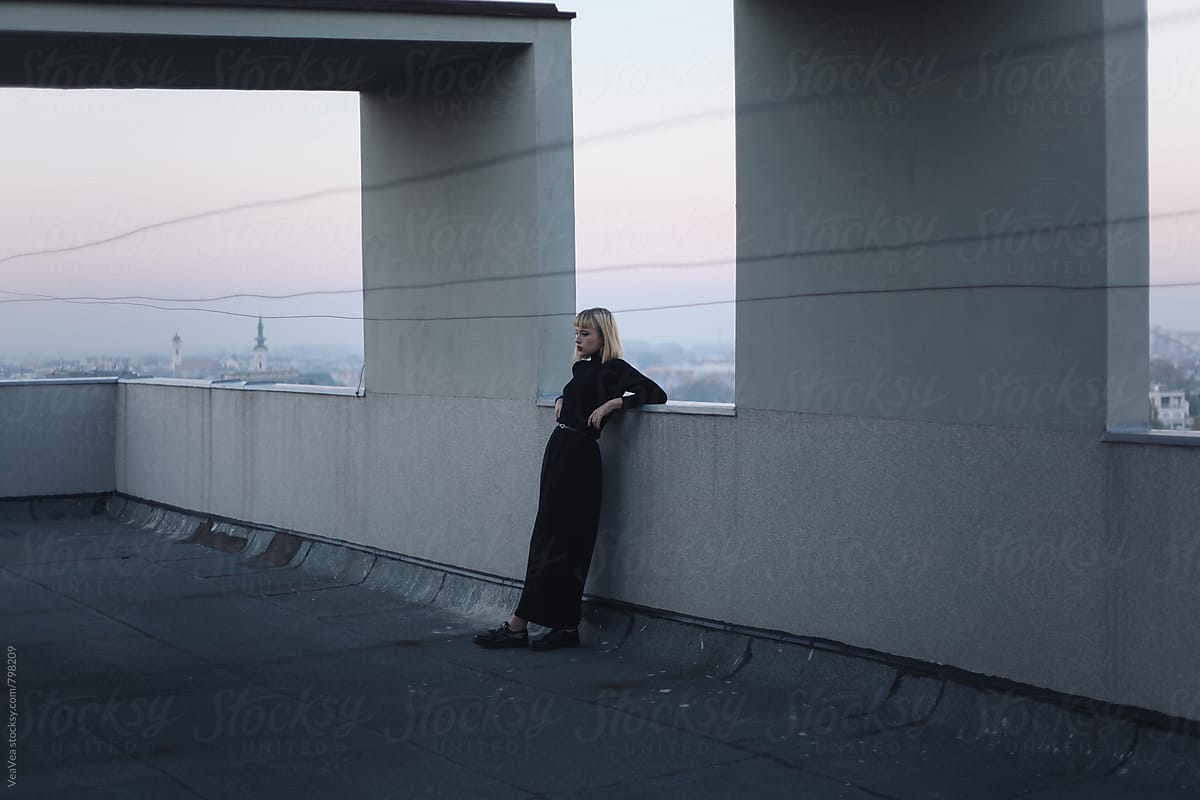 Stylish woman standing on the roof of the building during sunset