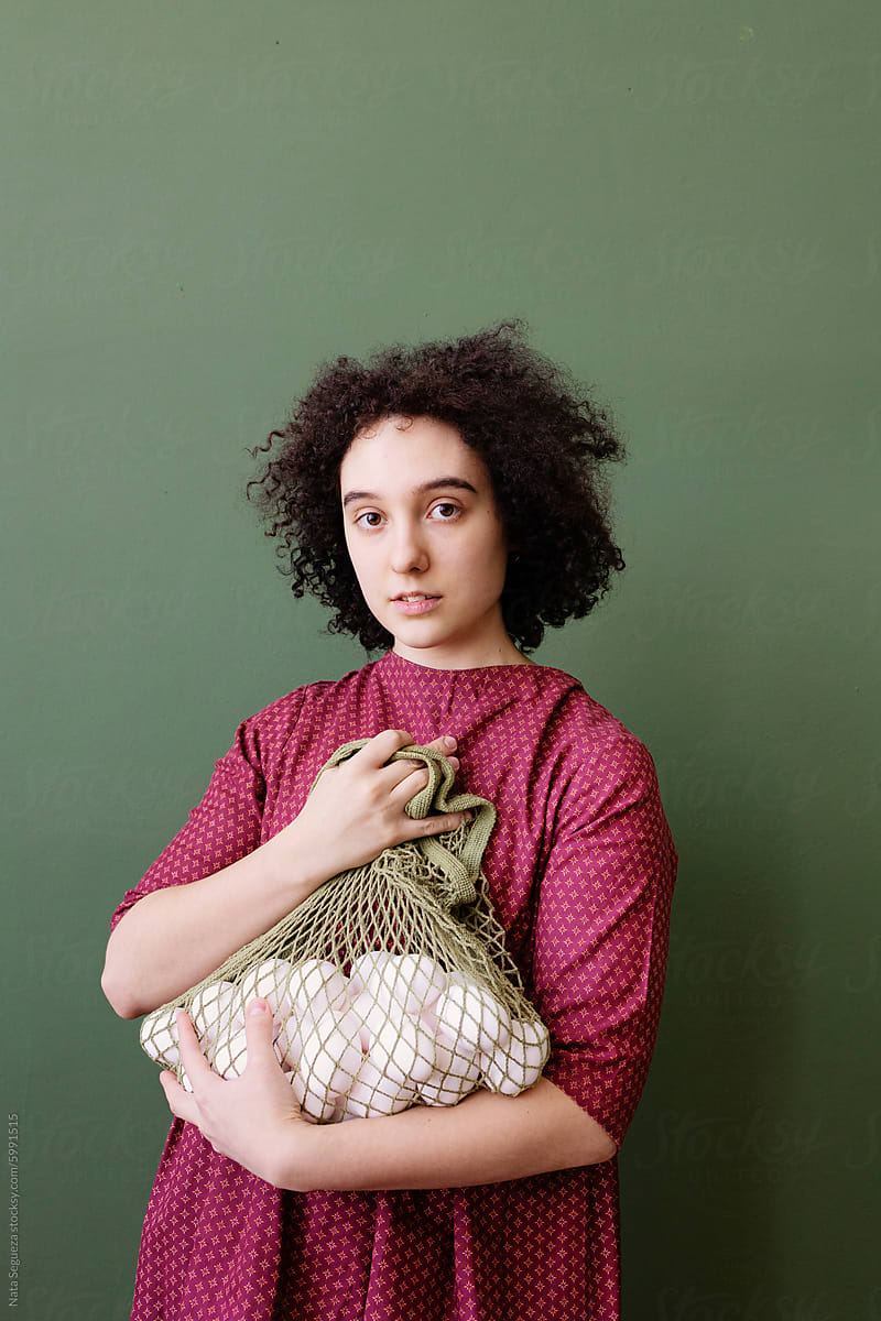 A girl holding a mesh bag full of eggs on a green background