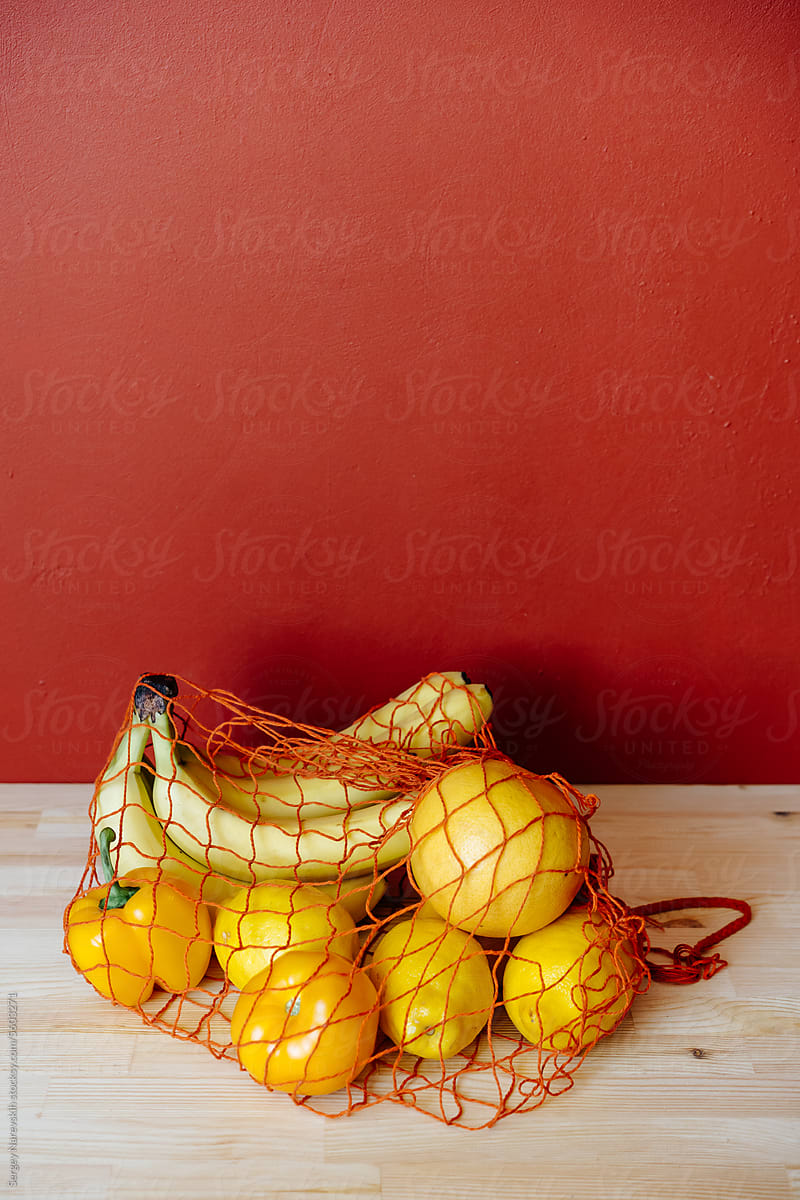 Yellow groceries in mesh bag against orange wall