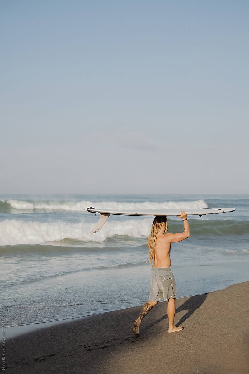 a guy with dreadlocks carries a surfboard on his head