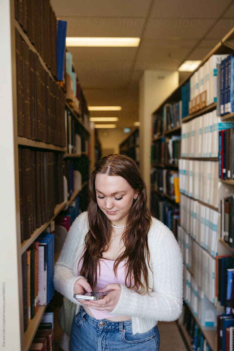 Young woman texting in library at college.