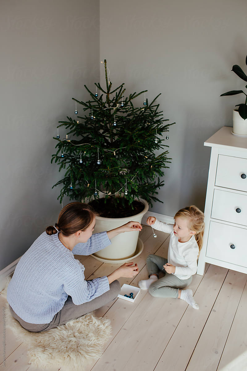Mother helping child decorating fir with glass bowls