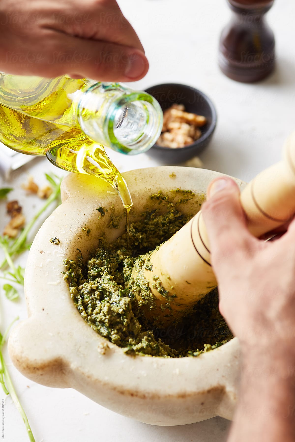 Hands adding olive oil in mortar