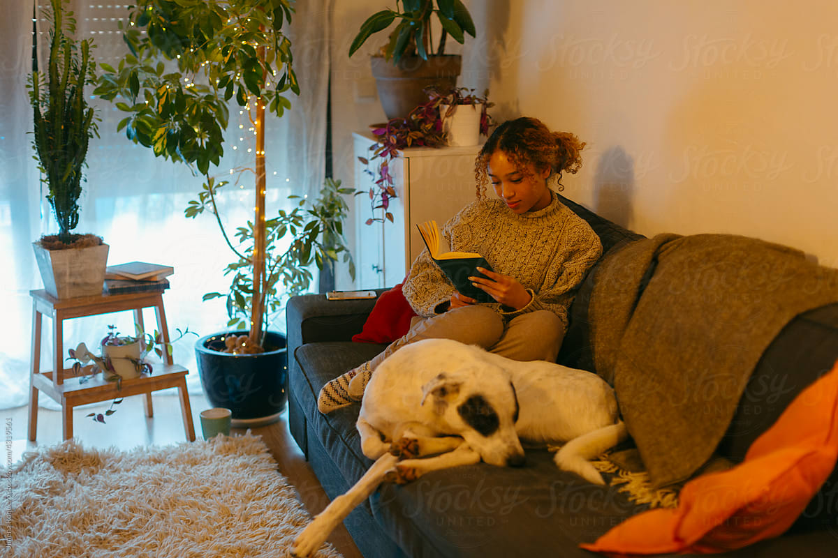Young woman reading on the couch with her dog