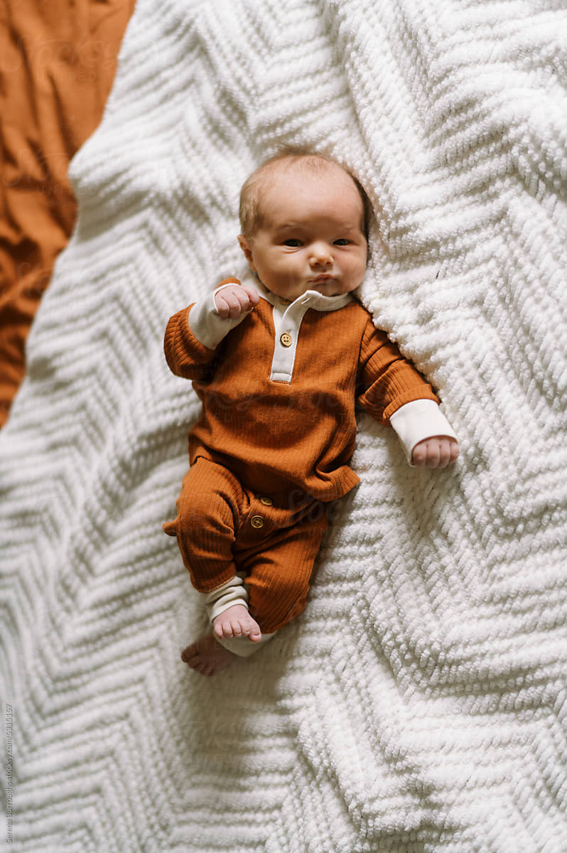 Awake newborn baby boy in orange clothing lying on bed at home