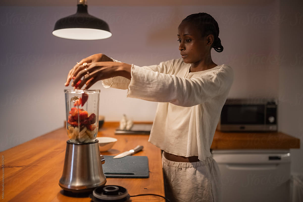 Black woman adding strawberries in blender