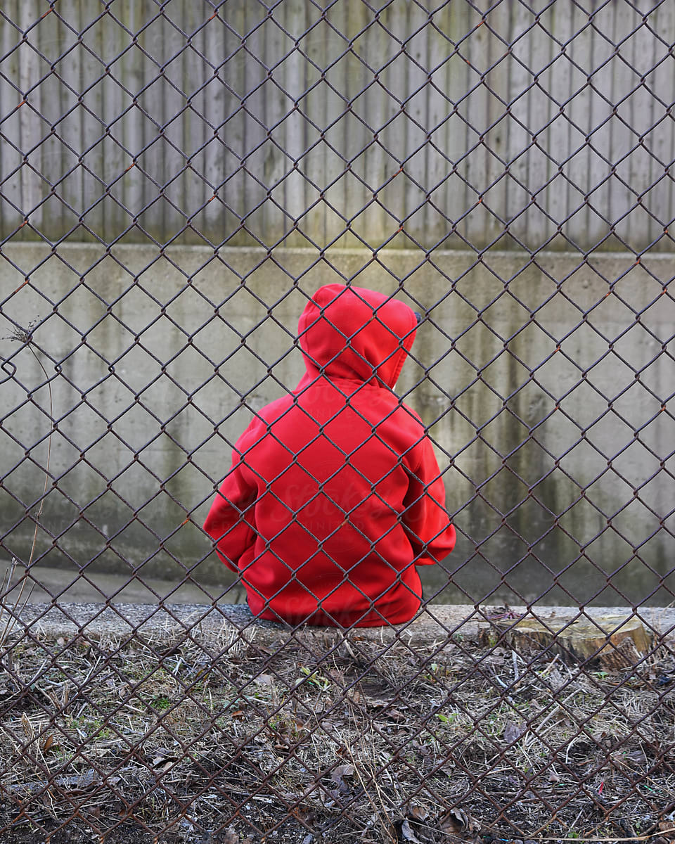 Boy in Red Alone and Sad Behind Fence
