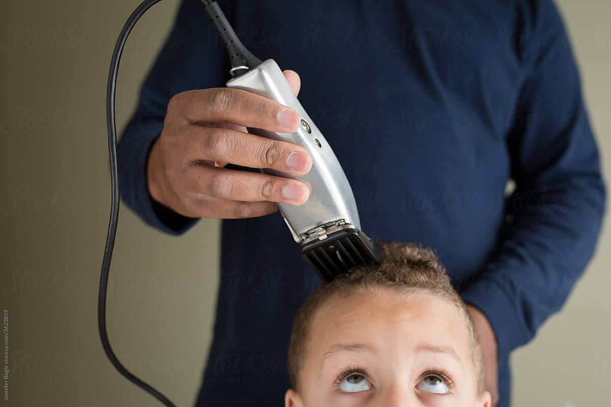 Man carefully clippers son\'\'s hair at home