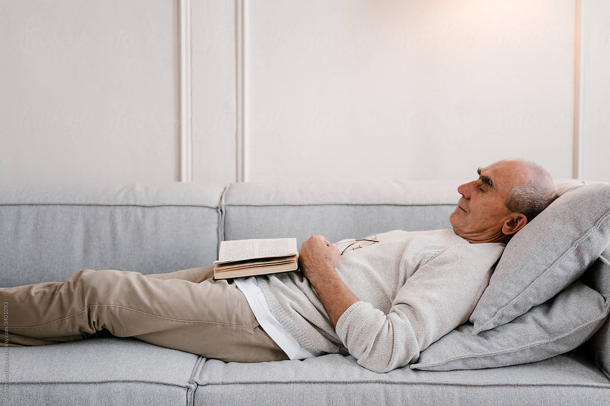 Senior man with book sleeping on sofa