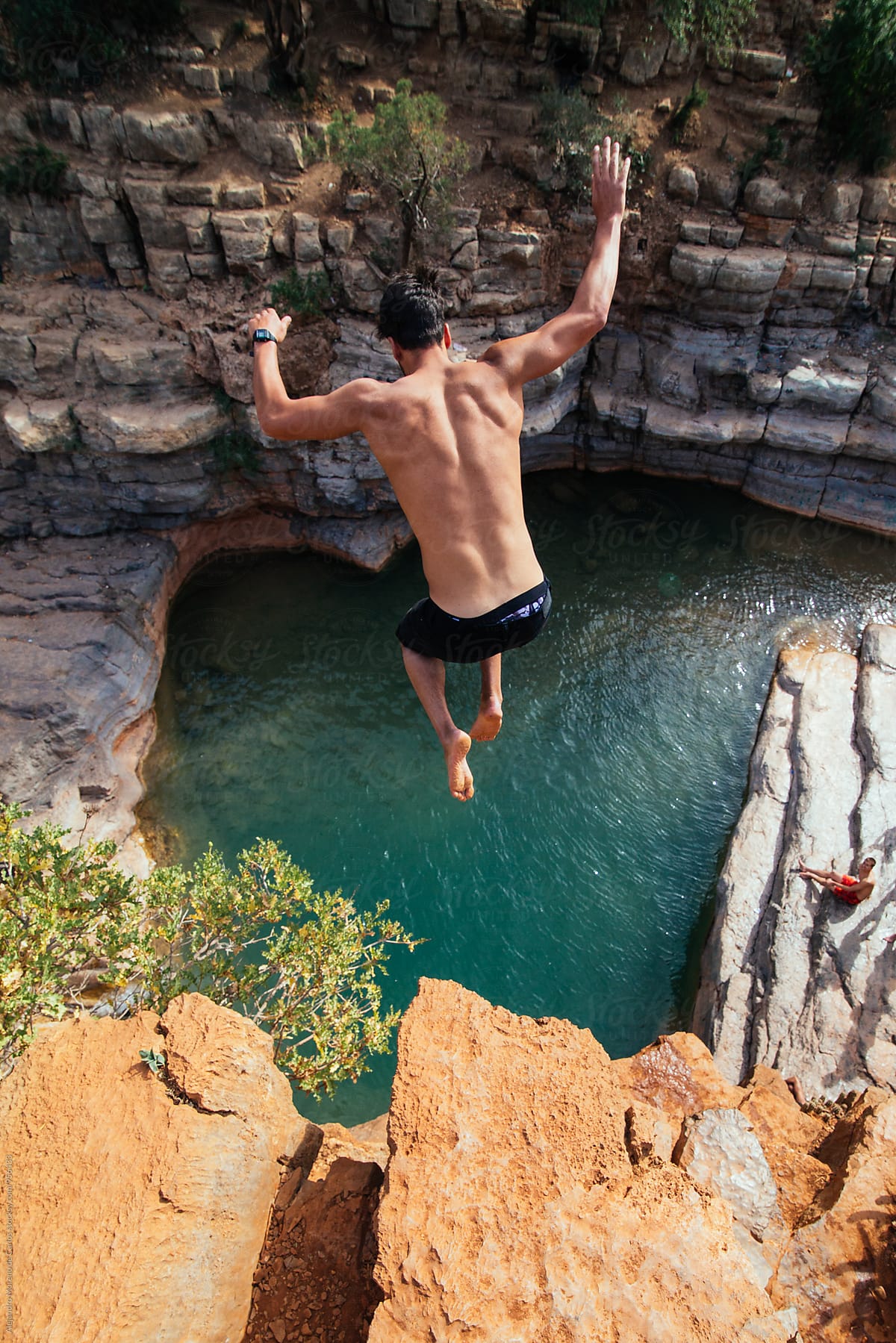 Close-up of black-haired man jumping from cliff to the water
