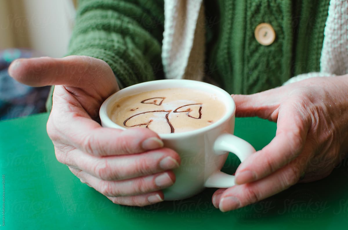 Hands holding a latte that is decorated with hearts
