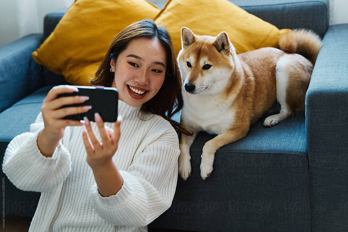 Smiling woman using mobile phone on the sofa with her dog.