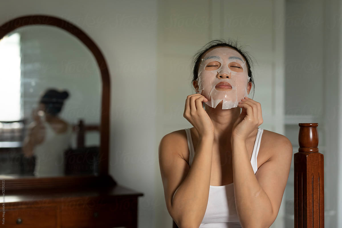 Portraiture of a young asian woman putting on a white prefabricated moisturised face-mask