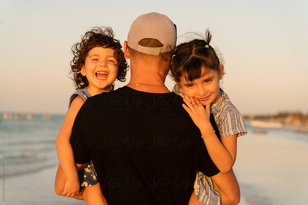 Father holding happy daughters on beach at sunset