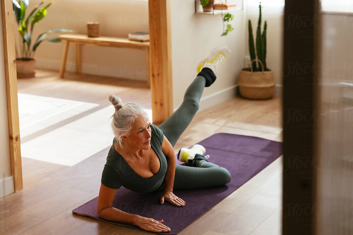Mature woman doing leg rise exercise on purple mat