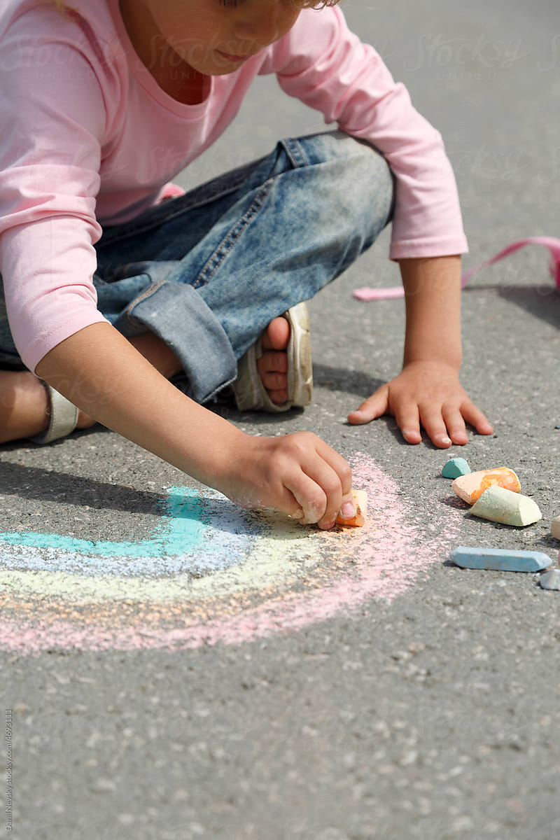 Crop child drawing rainbow with chalk in daytime