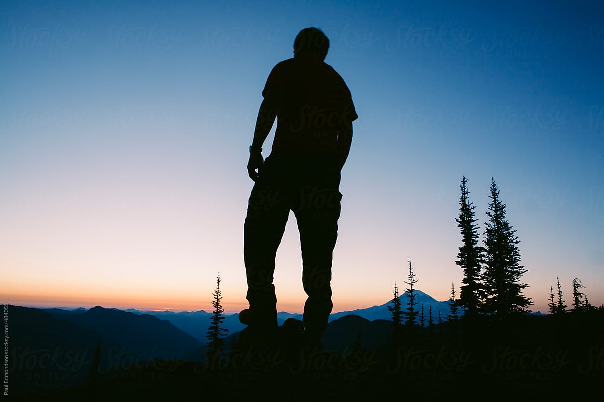 "Silhouette Of Man Standing On Mountain Summit At Dusk, Mt. Rainier In
