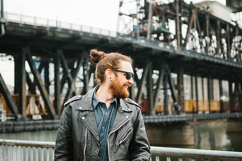 Hip man with red facial hair standing with bridge and cityscape