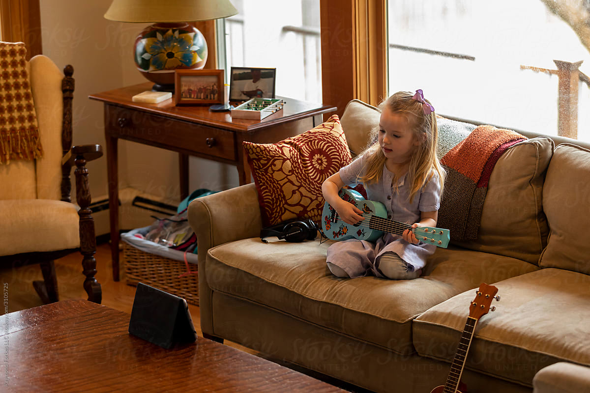 Young Child Learning to play Guitar Video Video Chat sitting in Living Room