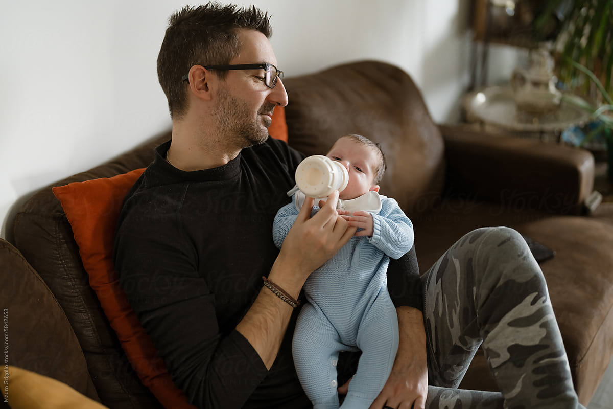 Man feeding his newborn baby with a bottle on the sofa
