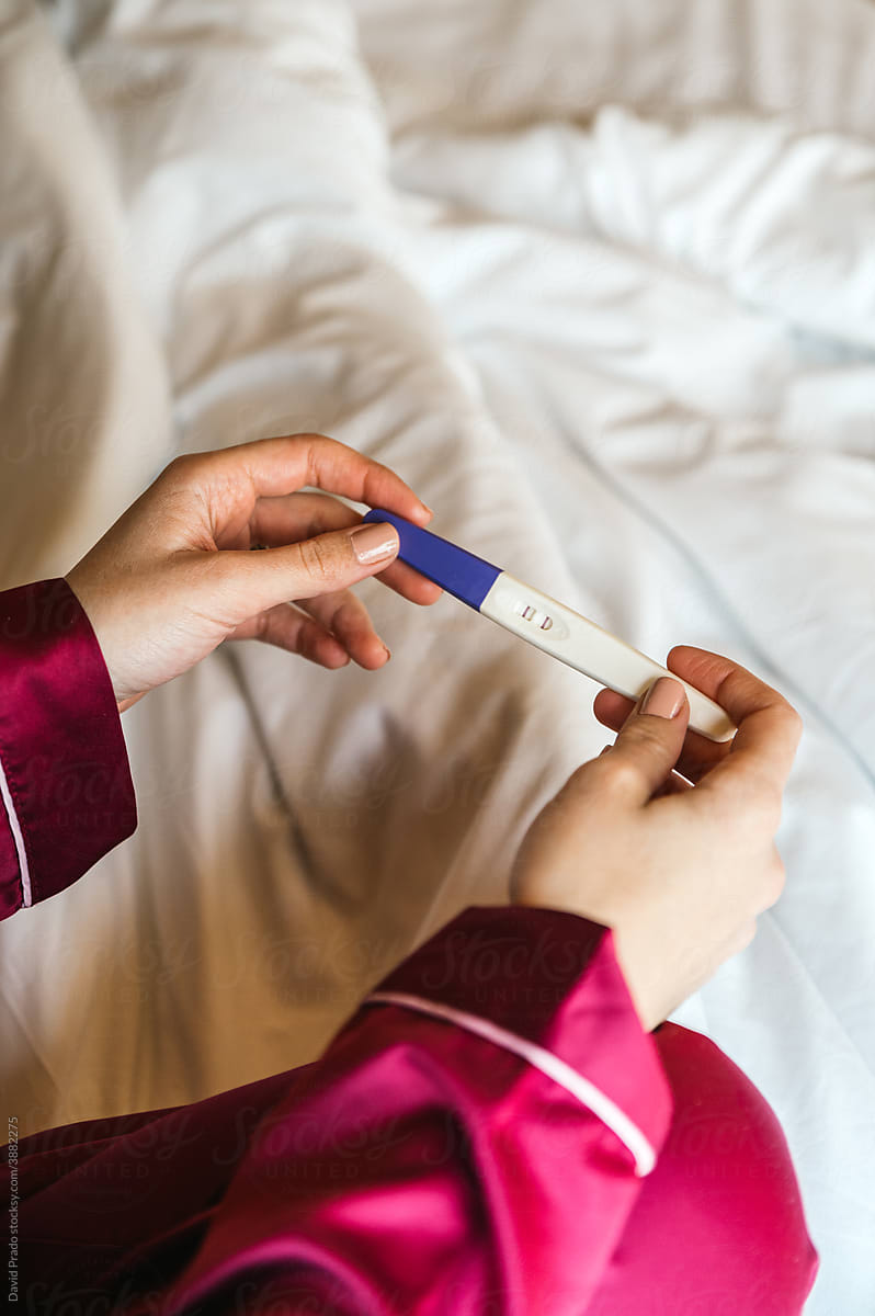 Woman with pregnancy test on bed
