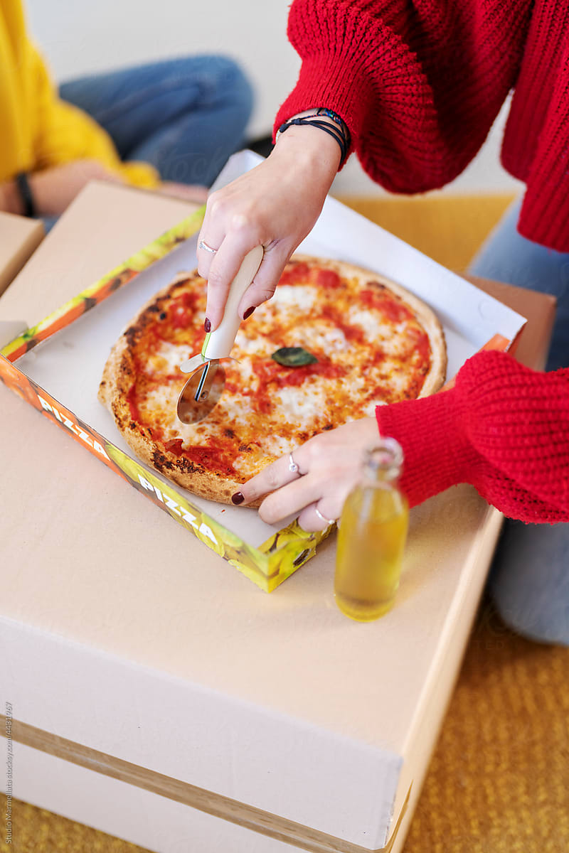 Woman cutting pizza on boxes in new apartment