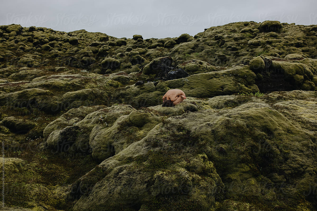 Young slim woman in fetal position on the green moss in Iceland