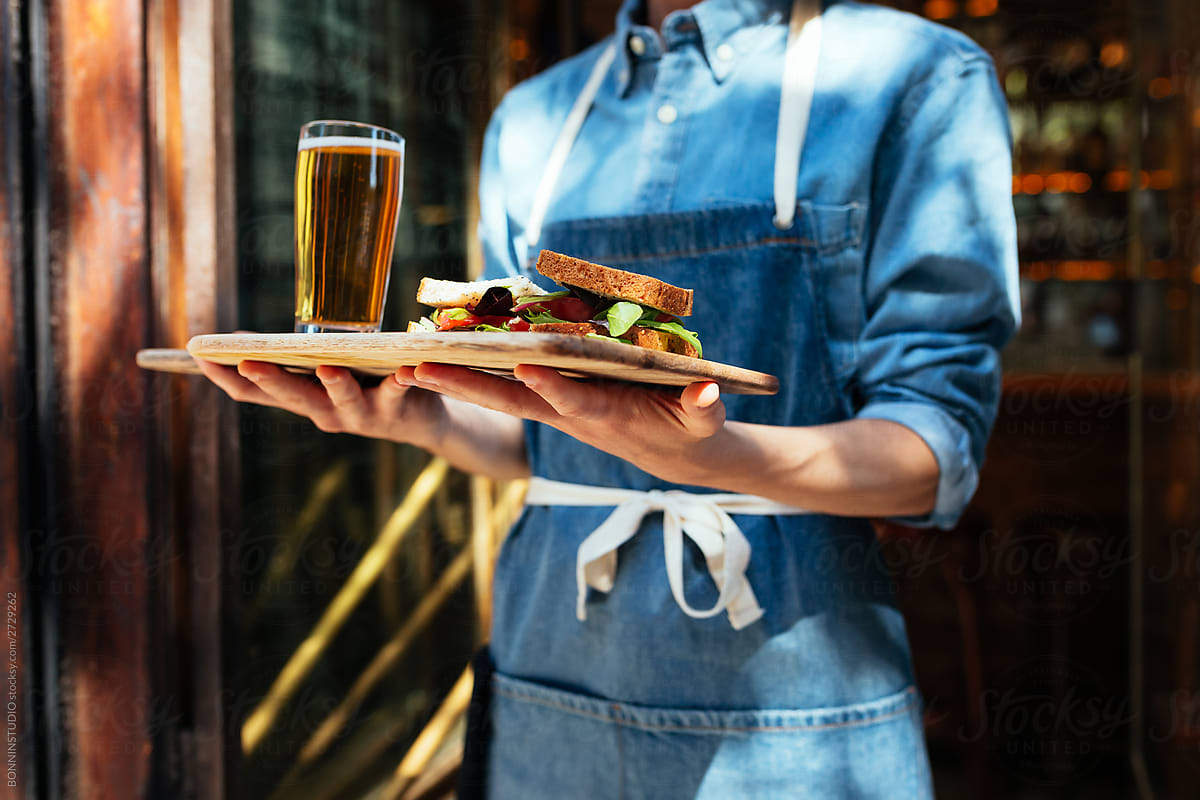 Crop waiter with beer and sandwich