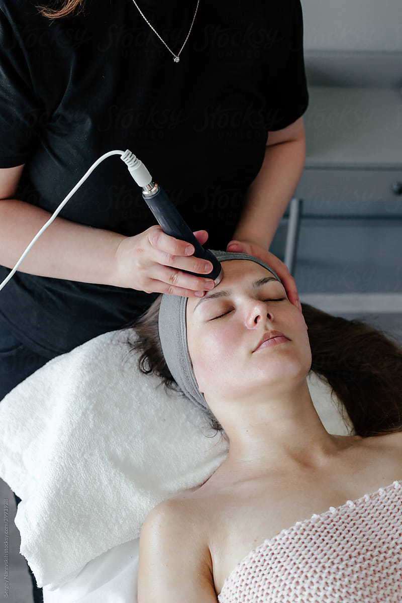 Crop female beautician doing ultrasonic massage to woman