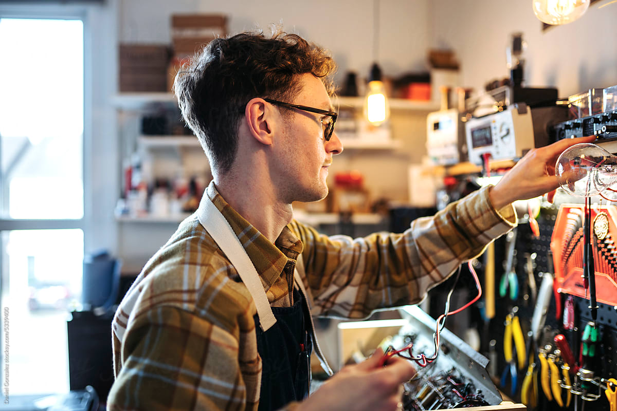 Young repairman working with electronics in own shop