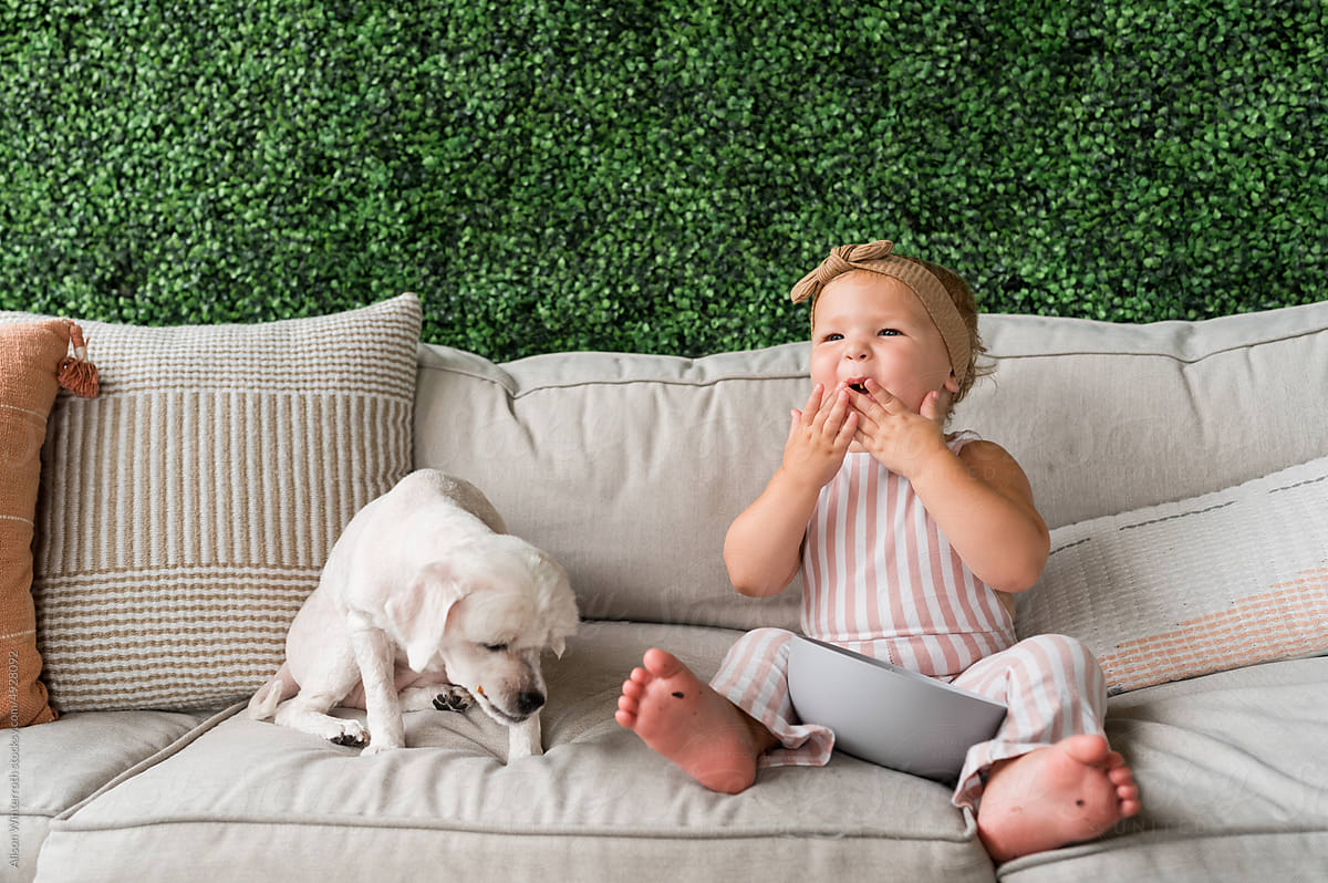Toddler and dog share a snack on couch