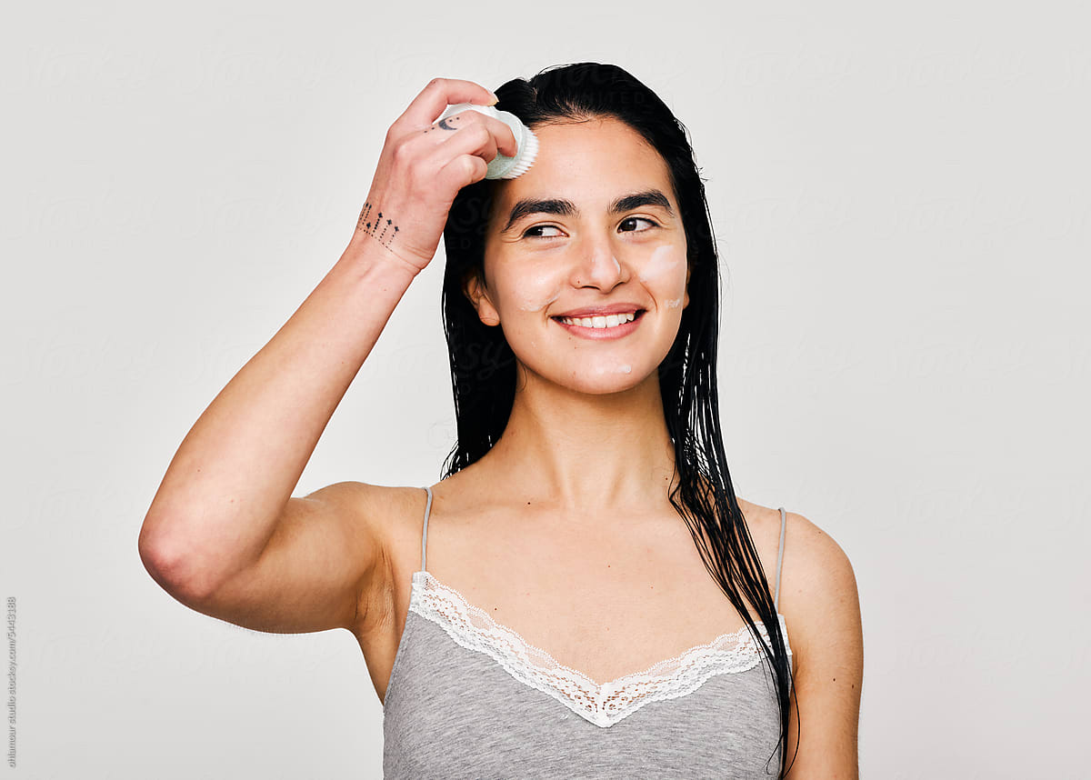 Woman smiling and washing her face with exfoliant brush