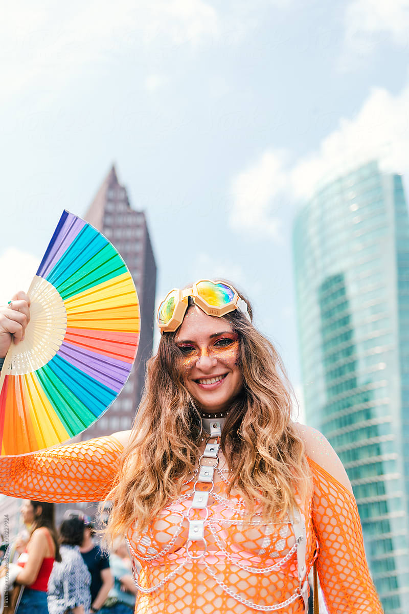 Cheerful colourful rave dressed up woman with rainbow fan at Pride