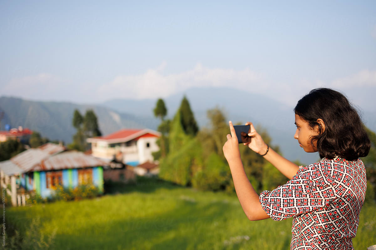 Young girl taking photo of a rural village in the hills