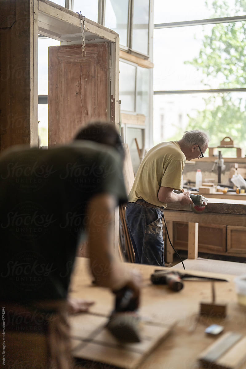 Two men sanding at the workshop and repairing old vintage furniture