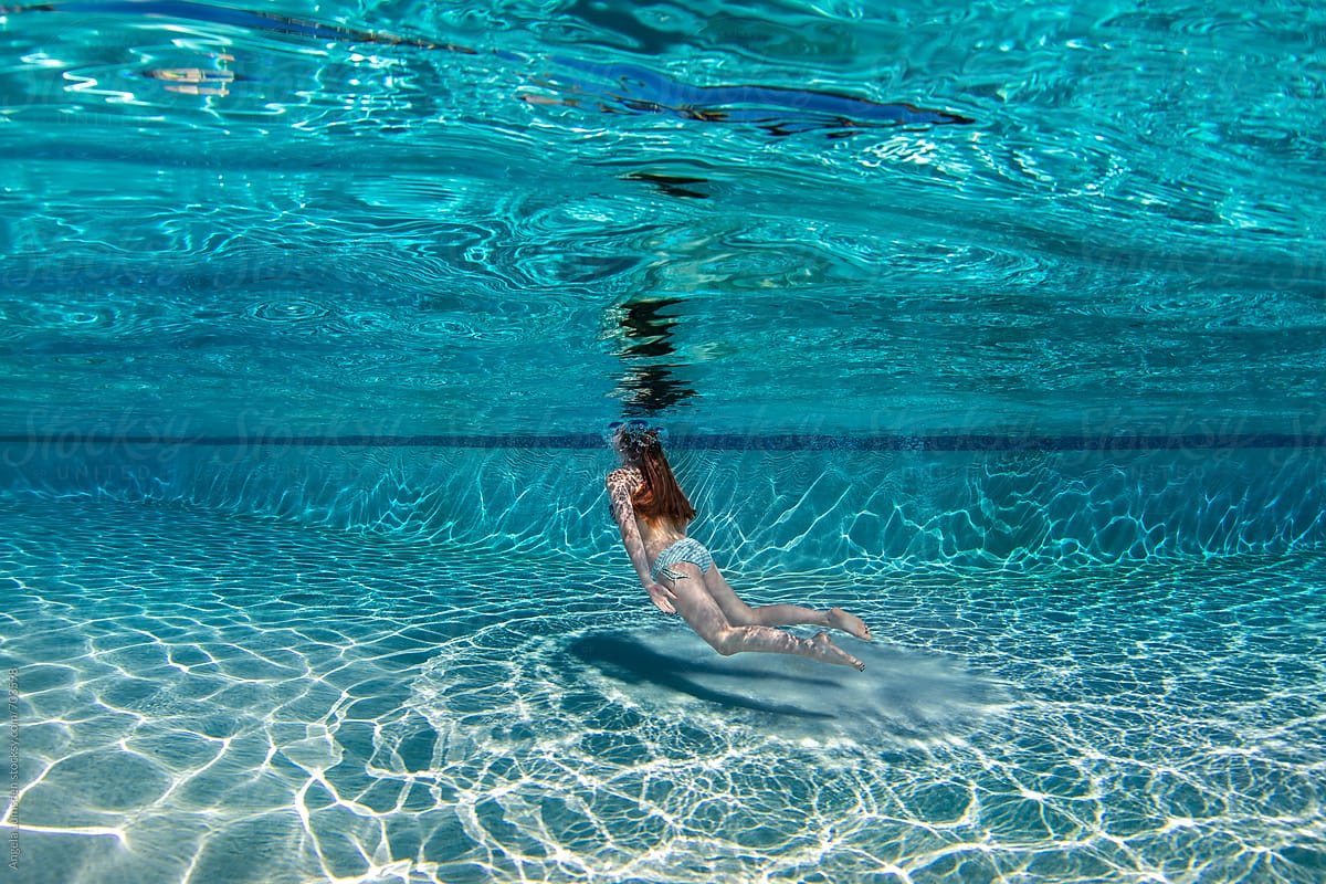 Teenage Girl Floating Underwater In A Large Deep Blue Swimming Pool By