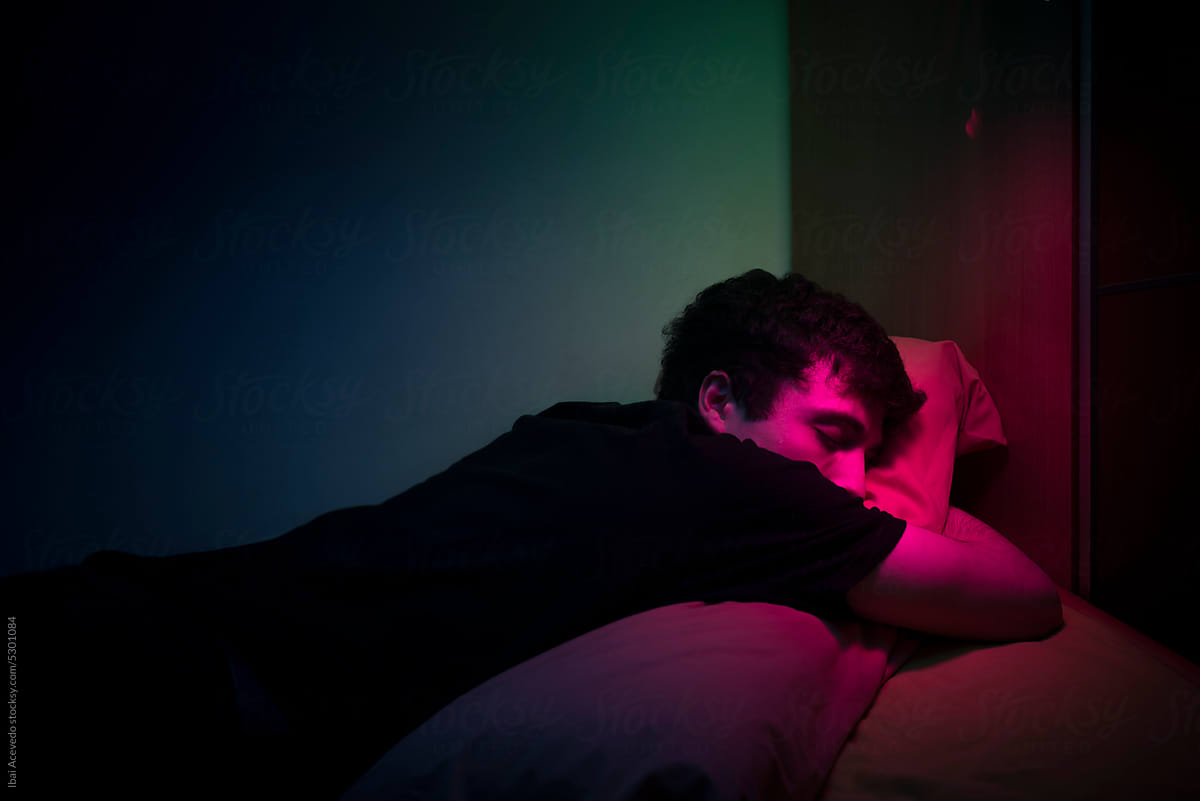 Young man sleeping on bed with dark neon lighting