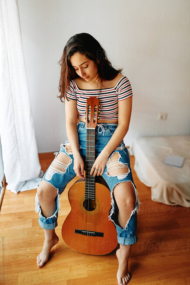Young woman sitting with an acoustic guitar in her apartment