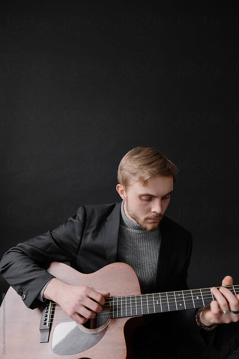 portrait of a guy in a stylish suit with a guitar in his hands, playing it