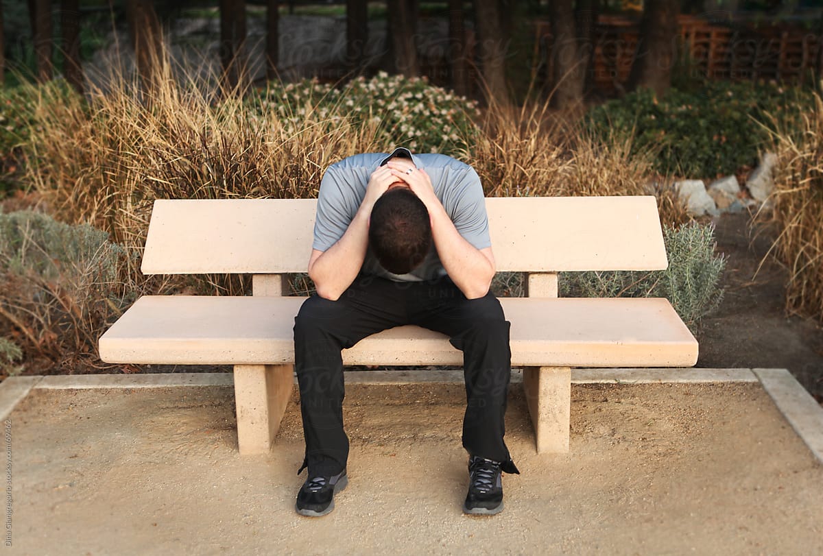 Man Sitting On Bench Outdoors With Head Down And Hands Clasped Behind Neck By Dina Giangregorio