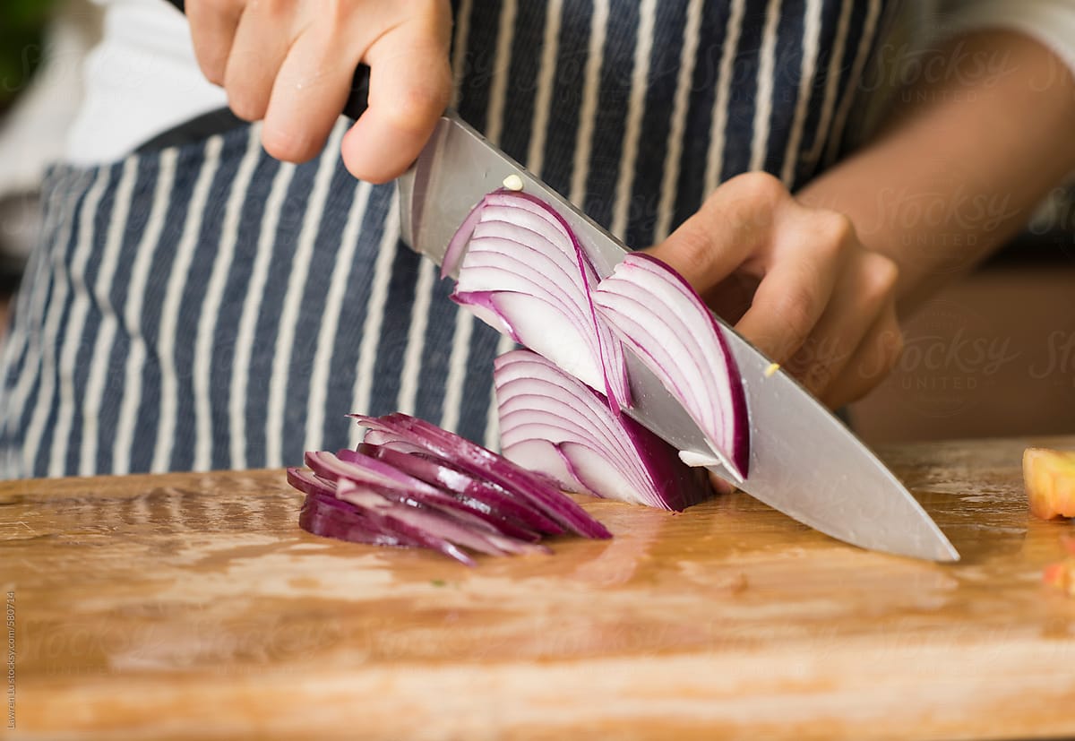 Female hands chopping red onion in kitchen background.