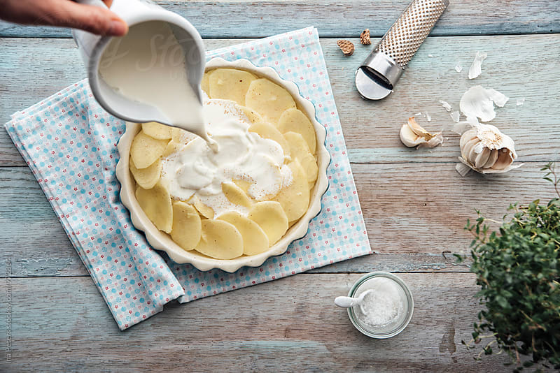 Food: Prearing gratinated potatos, pouring cream onto potatos