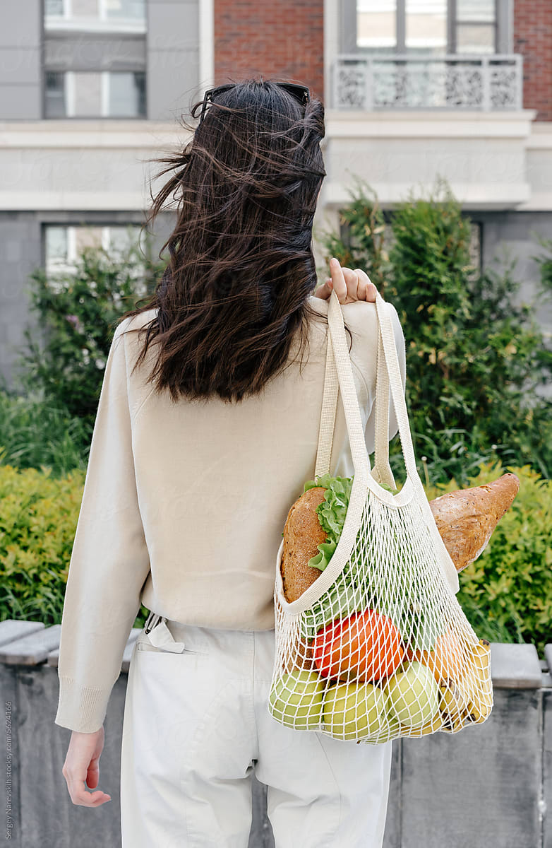 Back view of anonymous woman with mesh bag of groceries on shoulder