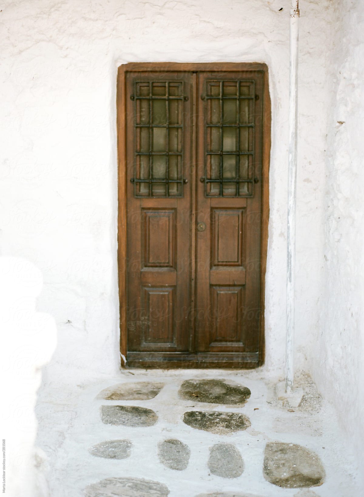 Old brown door with iron window grates with a cobble stone path