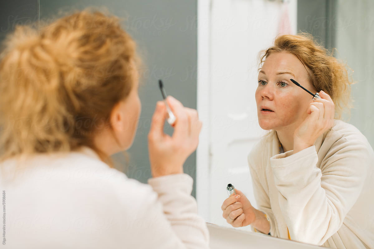 Woman applying mascara in front of a mirror