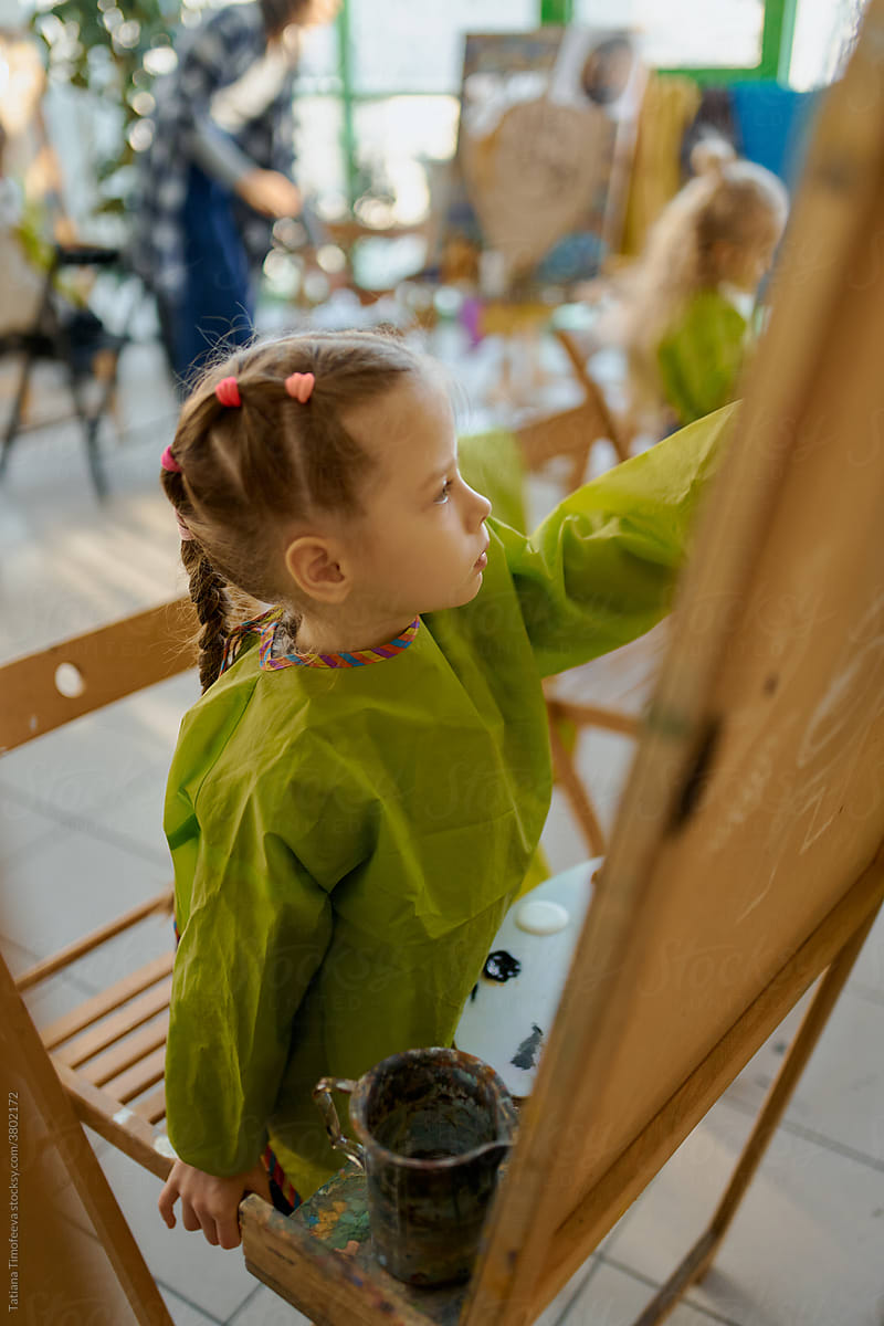 girl in uniform at a drawing class, drawing with paints at an easel